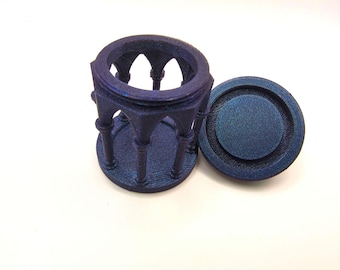 May include: A dark blue, openwork decorative object with a matching lid. The object has a cylindrical base with arched supports and a circular top. The lid is a flat disc with concentric circles. The object is likely a decorative container or holder.