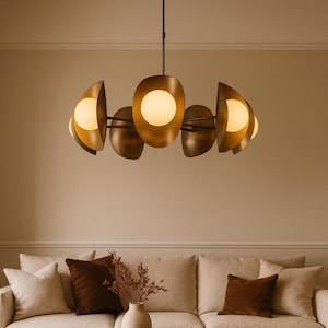 May include: A circular chandelier featuring multiple matte bronze, petal-shaped metal shades that each house a glowing, spherical white glass light bulb. The fixture is suspended from the ceiling by a thin, dark metal rod.