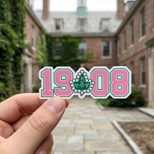 May include: A white ceramic mug with a black handle and the text "But First, Coffee" in a bold, black font. The mug is sitting on a wooden surface. The mug is approximately 4 inches tall.