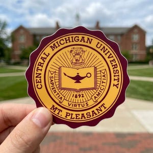 May include: A circular sticker featuring the Central Michigan University seal. The seal is in maroon and gold, with text that reads "Central Michigan University" and "Mt. Pleasant." The center features an open book and a lamp.