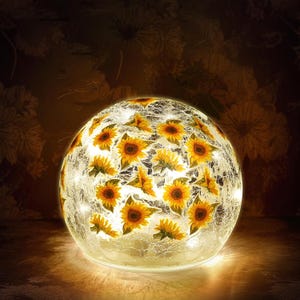 May include: A spherical decorative lamp featuring a mosaic design with yellow sunflowers. The lamp is illuminated from within, creating a warm, inviting glow. The glass has a crackled effect, adding to its unique aesthetic. The lamp is a decorative home accent.
