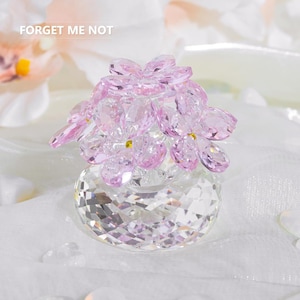 May include: A crystal flower sculpture with pink petals and a clear, faceted base. The sculpture is in the shape of a bouquet of flowers. The text "FORGET ME NOT" is visible in the background.