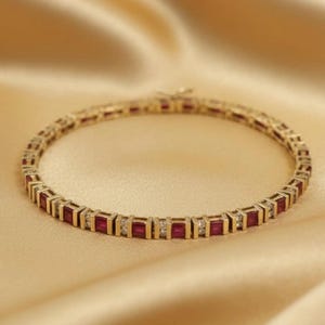 May include: A gold bracelet with square-cut red gemstones and small white gemstones. The bracelet is set against a gold-colored satin background. The bracelet is a piece of jewelry.
