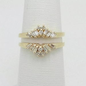 May include: A gold ring guard set featuring two matching bands, each adorned with a central cluster of small round diamonds flanked by tapered baguette-cut diamonds arranged in a fan-like pattern along the top edge of the yellow gold bands.