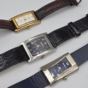 May include: Several rectangular wristwatches with leather bands are displayed. The watches have gold and silver-toned cases, with white, black, and blue faces. Roman numerals and hands indicate the time. The bands are brown, black, and blue.
