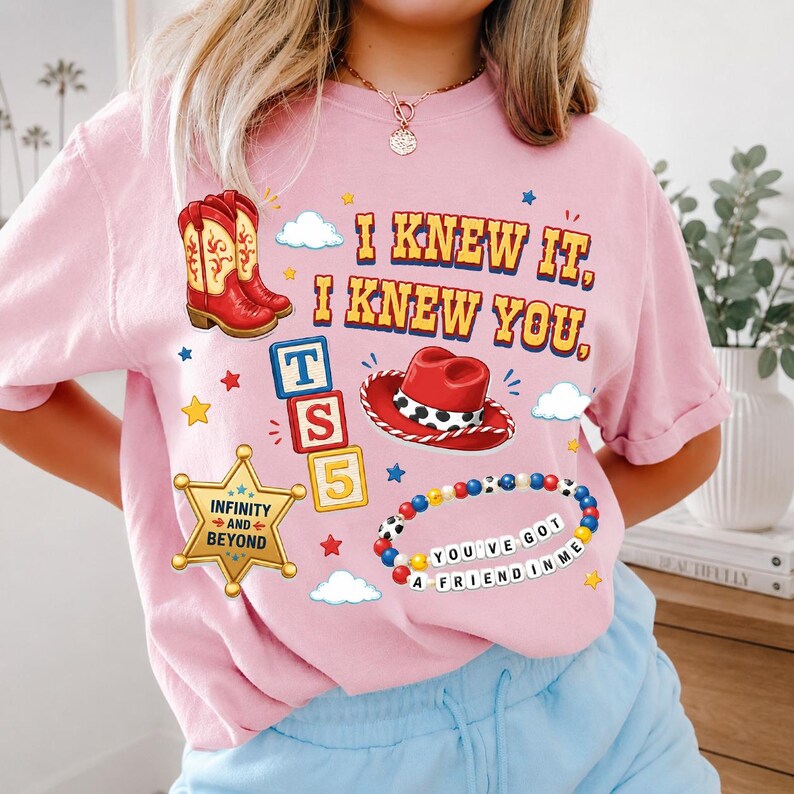 A woman wearing a pink t-shirt with various cartoon-style icons and text, including a cowboy boot, clouds, stars, and a bracelet.
