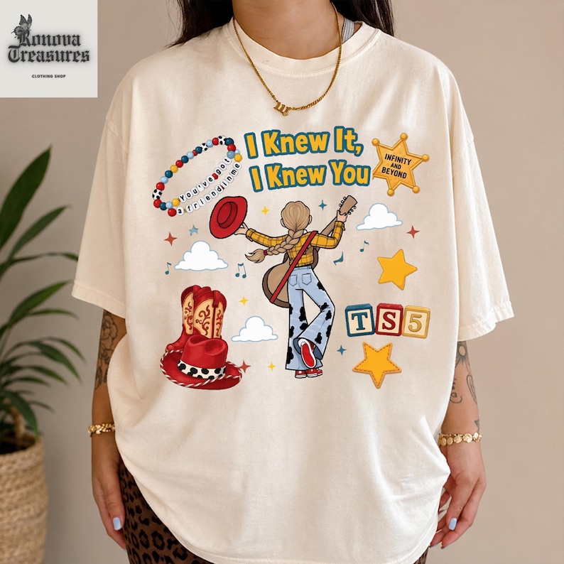A person wearing a white t-shirt with a graphic design featuring a cartoon character, a cowboy hat, and various other elements.