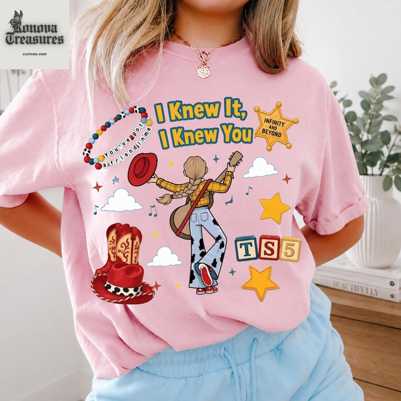 A woman wearing a pink t-shirt with various cartoon-style illustrations and text, including a cowboy hat, stars, and a guitar.
