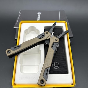 May include: A multi-tool set in a yellow box. The tools are tan and black, with a variety of functions. The set includes a black nylon sheath. The brand name "LEATHERMAN" is visible on the box.