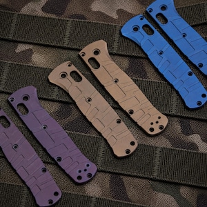 Puede incluir: Un juego de cinco cachas de repuesto para mangos de cuchillo con un patrón de rejilla geométrico. Las piezas se presentan en tres colores distintos: dos azules, dos marrones y una morada, todas con orificios pretaladrados para montaje.