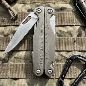 May include: A silver Leatherman Charge Titanium multi-tool with a partially deployed M390 steel blade. The handle features the embossed text LEATHERMAN CHARGE and TITANIUM. The tool is constructed with a textured metallic finish and exposed screws.