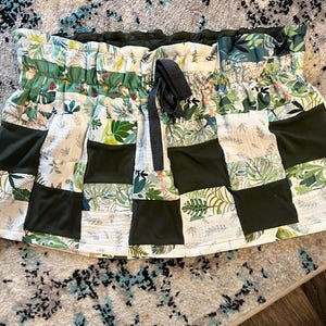 May include: A patchwork skirt in green, white, and dark green. It has a drawstring waist and a tropical leaf pattern. The skirt is constructed from multiple fabric squares. The skirt's design is reminiscent of a tropical theme.