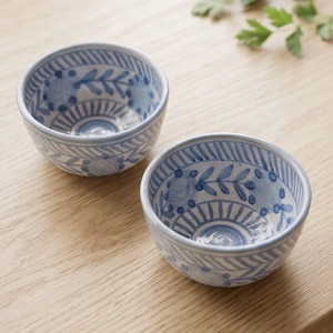 Könnte beinhalten: Zwei kleine, runde Keramikschalen mit blau-weißem Blumenmuster. Die Schalen haben ein detailliertes Design aus Blättern und Punkten mit einem hellblauen Rand. Die Schalen stehen auf einer hellen Holzoberfläche.