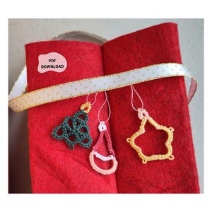 May include: Three small crocheted ornaments in dark green, red, and yellow hanging from a white and gold polka dot ribbon draped over a red felt surface. A pink label with the text PDF DOWNLOAD is visible on the upper left side of the felt.