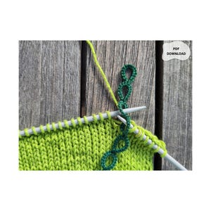 Könnte beinhalten: Ein helles lindgrünes Strickstück auf silbernen Stricknadeln mit einem dunkelgrünen dekorativen Schlaufenstichmuster, das in das Stück eingearbeitet wird. Ein weißes Etikett in der oberen rechten Ecke enthält den schwarzen Text PDF DOWNLOAD.
