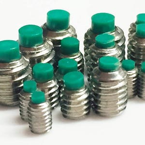 May include: A group of silver-coloured, threaded screws with bright green caps. The screws vary in size and are arranged closely together, creating a textured, industrial aesthetic. The green caps provide a contrasting pop of colour.