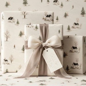May include: Three rectangular gift boxes wrapped in cream-colored paper featuring a repeating winter landscape pattern of houses, trees, and figures. The central box is tied with a wide, sheer taupe ribbon and a large bow, with a white gift tag.