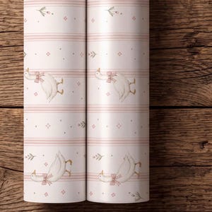May include: Two rolls of light pink wallpaper featuring a repeating pattern of white geese wearing pink bows, interspersed with small floral sprigs, tiny four-pointed stars, and horizontal stripes in varying shades of soft pink and white.