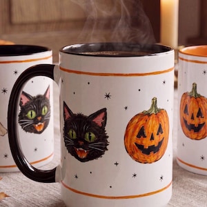 Peut inclure: Un mug en céramique blanche avec une anse et un intérieur noirs, orné d'un motif répétitif de têtes de chats noirs aux yeux verts et de citrouilles d'Halloween orange, agrémenté de petites étoiles et points noirs, avec des bandes orange.