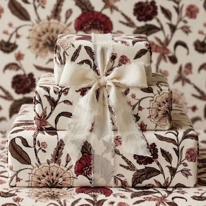 Könnte beinhalten: Drei Geschenkboxen, verpackt in floral gemustertem Papier mit einer cremefarbenen Schleife. Die Boxen sind übereinander gestapelt. Das Blumenmuster umfasst Burgunder-, Braun- und Cremefarben.