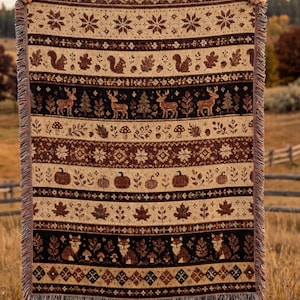 Peut inclure: Un plaid tissé rectangulaire présentant des bandes horizontales de motifs sur le thème de l'automne dans des tons marron, crème et noir. Le design comprend des motifs d'écureuils, de cerfs, de citrouilles, de renards, de champignons et de feuilles.