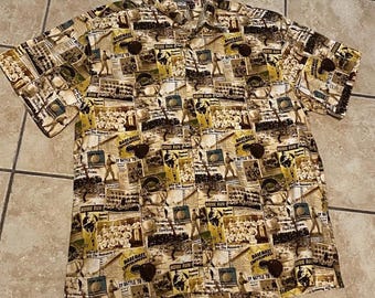 May include: Tan button-down shirt with a baseball-themed print. The shirt features a collage of baseball images, newspaper clippings, and the words "HOME RUN" and "DY BATTLE TO". The shirt has short sleeves and brown buttons.
