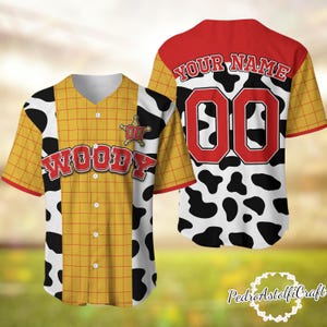 A baseball jersey with a cow print pattern and the name "Woody" printed on it. The jersey has a red and white color scheme and the number "00" printed on the back.