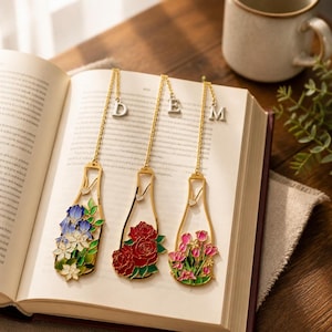 Puede incluir: Tres marcapáginas decorativos de metal con forma de botellas de vino, cada uno con un diseño floral diferente: iris azules, rosas rojas y tulipanes rosas. Los marcapáginas cuelgan de cadenas doradas con letras plateadas.