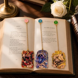 Puede incluir: Tres marcapáginas de metal con cadenas doradas y dijes circulares con las letras K, S y T. Cada marcapáginas tiene un colgante rectangular decorado con intrincados motivos de mariposas y flores en paletas de colores rojo, azul y dorado.