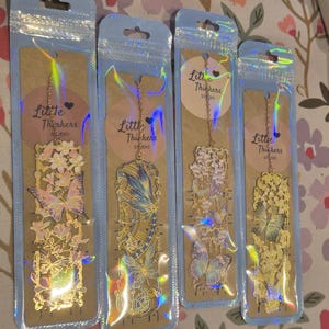 Set of four custom-initial gold-tone metal bookmarks with butterfly and floral filigree, personalized, in blue packaging.