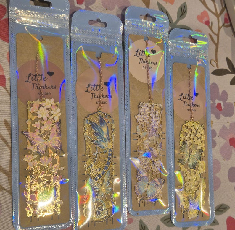 Set of four custom-initial gold-tone metal bookmarks with butterfly and floral filigree, personalized, in blue packaging.