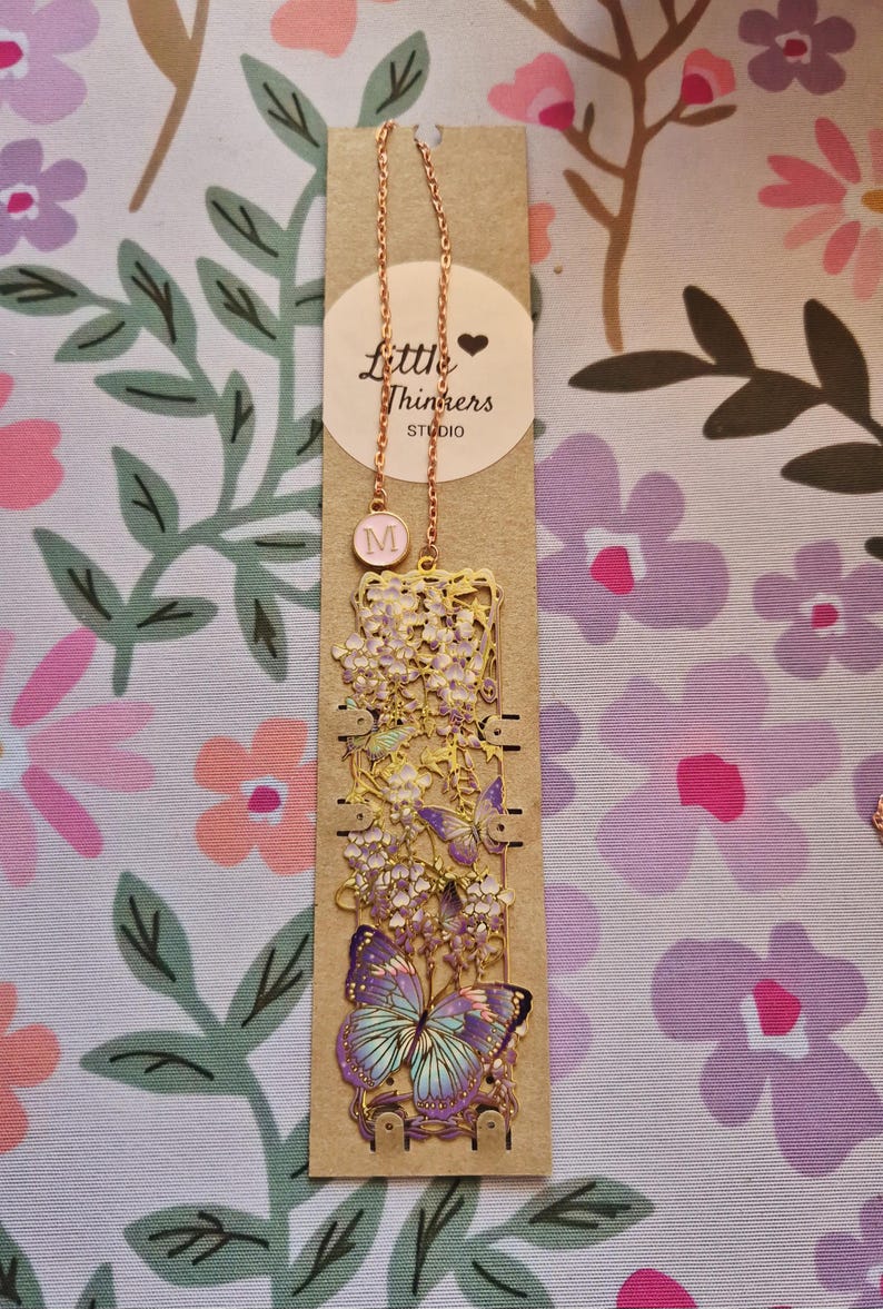 Set of four custom-initial gold-tone metal bookmarks with butterfly and floral filigree, personalized, in blue packaging.