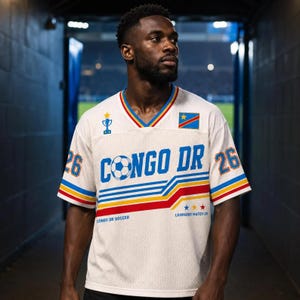 May include: A white mesh soccer jersey featuring the text CONGO DR in blue, a soccer ball graphic, and the number 26 on the sleeves. The shirt includes a blue, yellow, and red striped pattern, a trophy icon, the Congo flag, and text reading LEOPARDS MATCH 26.