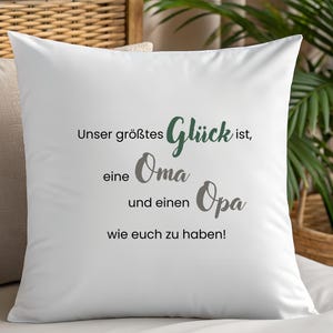 May include: White throw pillow with text in German. The text reads "Unser größtes Glück ist, eine Oma und einen Opa wie euch zu haben!" in black, gray, and green lettering. The pillow is on a white surface.