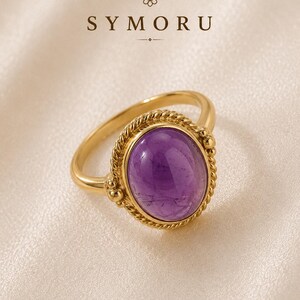 May include: A gold ring with a large, oval purple amethyst gemstone. The ring has a twisted rope design around the gemstone and a smooth band. The word "SYMORU" is printed in brown at the top of the image.
