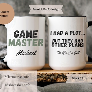 Könnte beinhalten: Weiße Keramik-Tasse mit schwarzem Griff und Rand. Auf der Vorderseite steht "GAME MASTER" mit einem Namen darunter. Auf der Rückseite steht "I HAD A PLOT... BUT THEY HAD OTHER PLANS The life of a GM". Mikrowellen- und spülmaschinenfest.