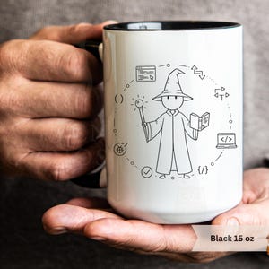 May include: White ceramic mug with a black interior and handle. The mug features a black and white illustration of a wizard holding a wand and book, surrounded by coding symbols. The text "Black 15 oz" is at the bottom.