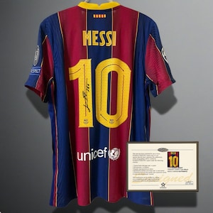 以下が含まれることがあります： バルセロナのサッカーユニフォーム。名前「MESSI」と番号「10」が金色の文字で書かれています。ユニフォームは主に青とマルーンで、黄色の襟が付いています。「unicef」のロゴとサインがあります。