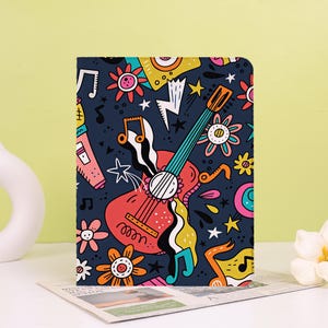 May include: A rectangular tablet case featuring a dark blue background with a colorful pattern of a red acoustic guitar, musical notes, stylized flowers, yellow stars, and white lightning bolts. The design is vibrant and covers the entire front surface.