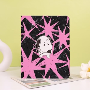 Könnte beinhalten: Eine rechteckige Tablet-Hülle mit schwarzem Hintergrund in Used-Optik und einem Muster aus leuchtend pinken Sternen. In der Mitte befindet sich ein weißer Cartoon-Hund mit schwarzer Nase und einem skeptischen Gesichtsausdruck.