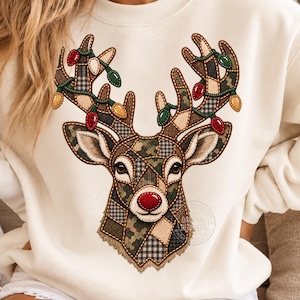 Könnte beinhalten: Ein cremefarbenes Sweatshirt mit Rundhalsausschnitt und einer großen Grafik eines Hirschkopfes. Der Hirsch besteht aus verschiedenen Patchwork-Mustern in Grün-, Braun- und Beigetönen, mit einer leuchtend roten Nase und einem Geweih voller Lichter.