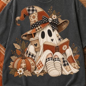 May include: A charcoal gray t-shirt featuring a graphic of a ghost wearing a patchwork witch hat, reading a book, and holding a coffee cup. The ghost is surrounded by a pumpkin, autumn leaves, and wears cozy socks, all rendered in a rustic, textured style.