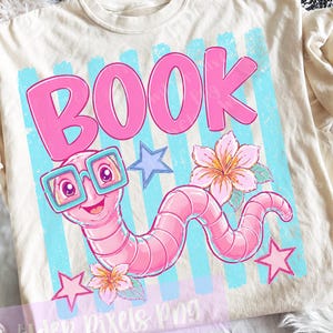 May include: Cream-colored t-shirt featuring a cartoon worm wearing glasses, with the word "BOOK" in pink. The design includes blue stripes, stars, and flowers. A fun, whimsical design for book lovers.