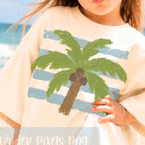 May include: Cream-colored t-shirt featuring a green palm tree design with a brown trunk and blue stripes. The text "Wilder Pixels Png" is printed at the bottom. The shirt is worn by a person wearing sunglasses.