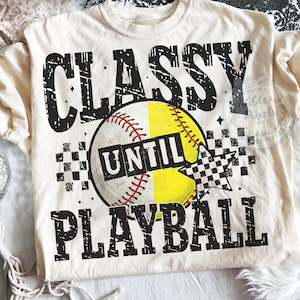 May include: Cream-colored t-shirt with the text "CLASSY UNTIL PLAYBALL" in distressed black font. A baseball graphic is in the center, split between white and yellow, with red stitching. A checkered flag graphic is on the right.