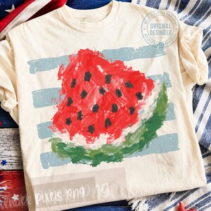 May include: A cream-coloured t-shirt featuring a painterly graphic of a watermelon slice with red flesh, black seeds, and a green rind. The design is layered over horizontal light blue brushstrokes. A circular watermark reads Original Desinger.