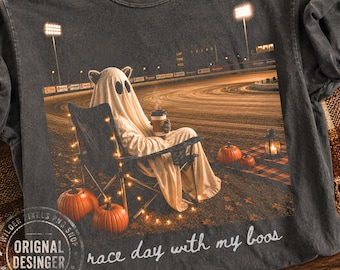 Puede incluir: Una camiseta gris carbón de cuello redondo con un gráfico de un fantasma sentado en una silla plegable en una pista de carreras, sosteniendo un café. La escena incluye calabazas, luces y el texto race day with my boos en color blanco.