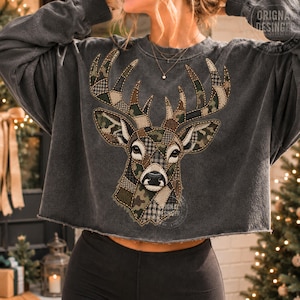 Könnte beinhalten: Ein anthrazitfarbenes Langarm-Sweatshirt mit offenem Saum und einem großen, zentralen Hirschkopf-Motiv. Der Hirsch besteht aus verschiedenen Patchwork-Mustern, darunter Camouflage, Karomuster und einfarbige braune Stoffstrukturen.
