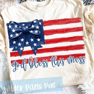 May include: Cream-colored t-shirt featuring a patriotic design. The design includes a blue bow with white stars, red and white stripes, and the phrase "God bless this mess" in blue script. A festive tee for Independence Day.
