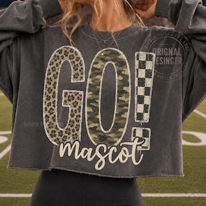 May include: A charcoal gray cropped sweatshirt featuring the text GO! in large letters. The G has a leopard print, the O has a camouflage pattern, and the exclamation point has a black and white checkerboard pattern. The word mascot is below.